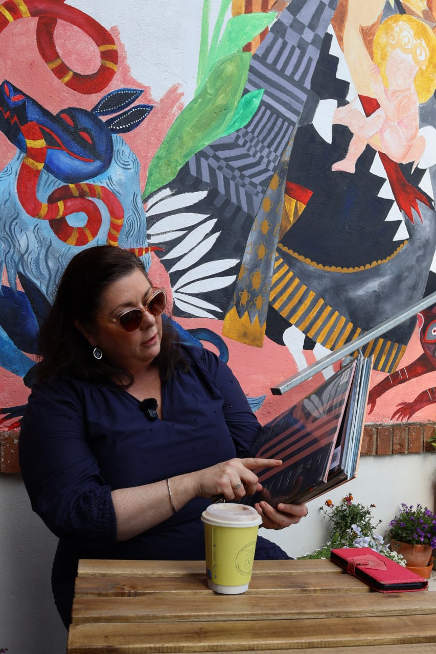 Elizabeth Stack seated outdoors in front of a colourful mural during a Kilmorna Collection interview