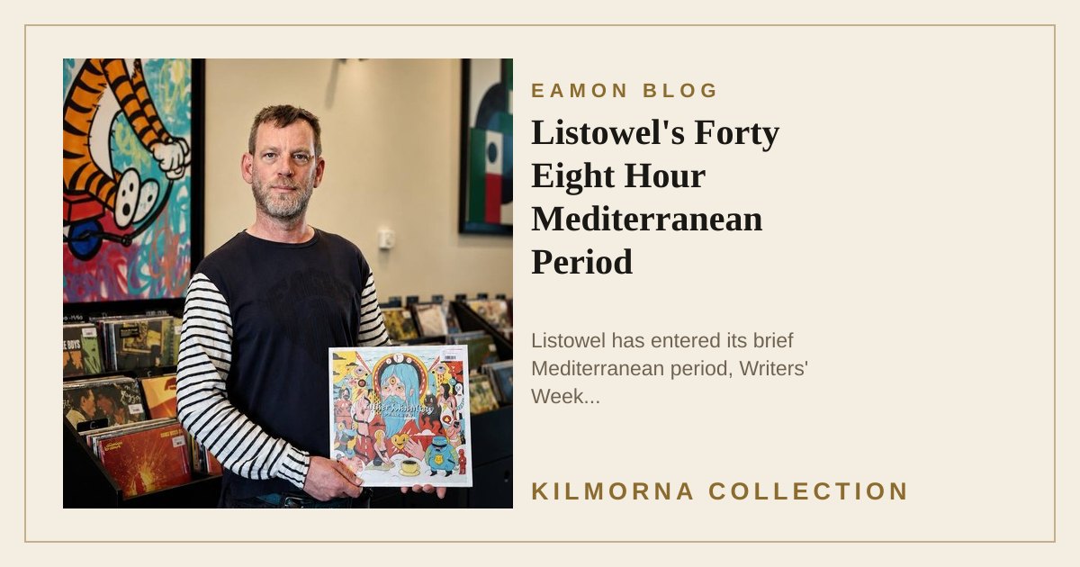 Eamon Lane standing inside The Kilmorna Collection holding a colourful vinyl record, with framed art and record shelves behind him